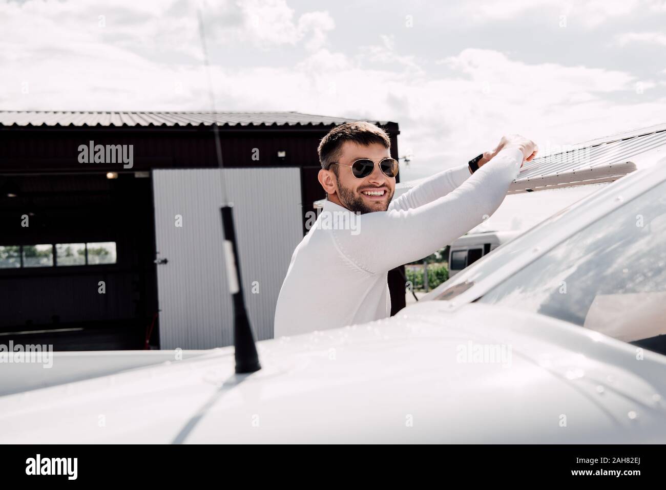 Sorridente uomo barbuto in occhiali da sole in piedi vicino a piano nella giornata di sole Foto Stock