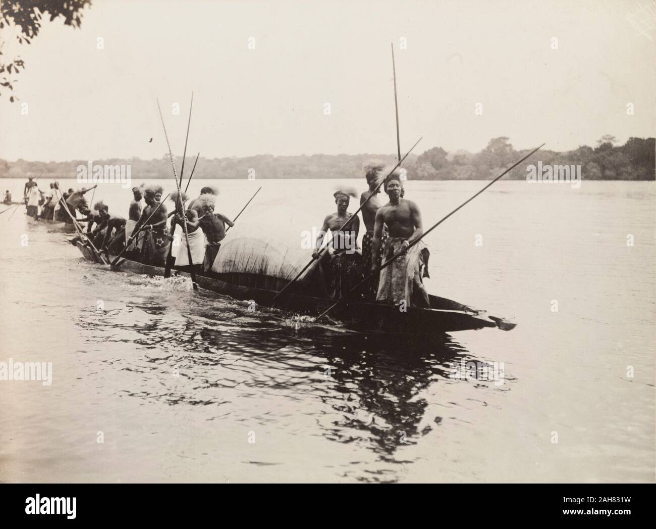 ZambiaNorthern Rhodesia, un gruppo di uomini africani che indossano costumi tradizionali e copricapo paddle canoe passato Kandahar Isola, Rhodesia settentrionale (Zambia), 13 novembre 1910.Note da stampato un itinerario di visita:Domenica, Novembre 13mattina. Palazzo del Governo, il servizio divino.1 P.M il pranzo. Valutazione: Il curato. Eventualmente anche il Vescovo di Rhodesia settentrionale.4 P.M. A Fiume e nel lancio di Kandahar Island, dove il tè sarà presa.8 P.M. La sede del governo, cena privata, non ospiti, 1910. 1995/076/1/4/1/68. Foto Stock