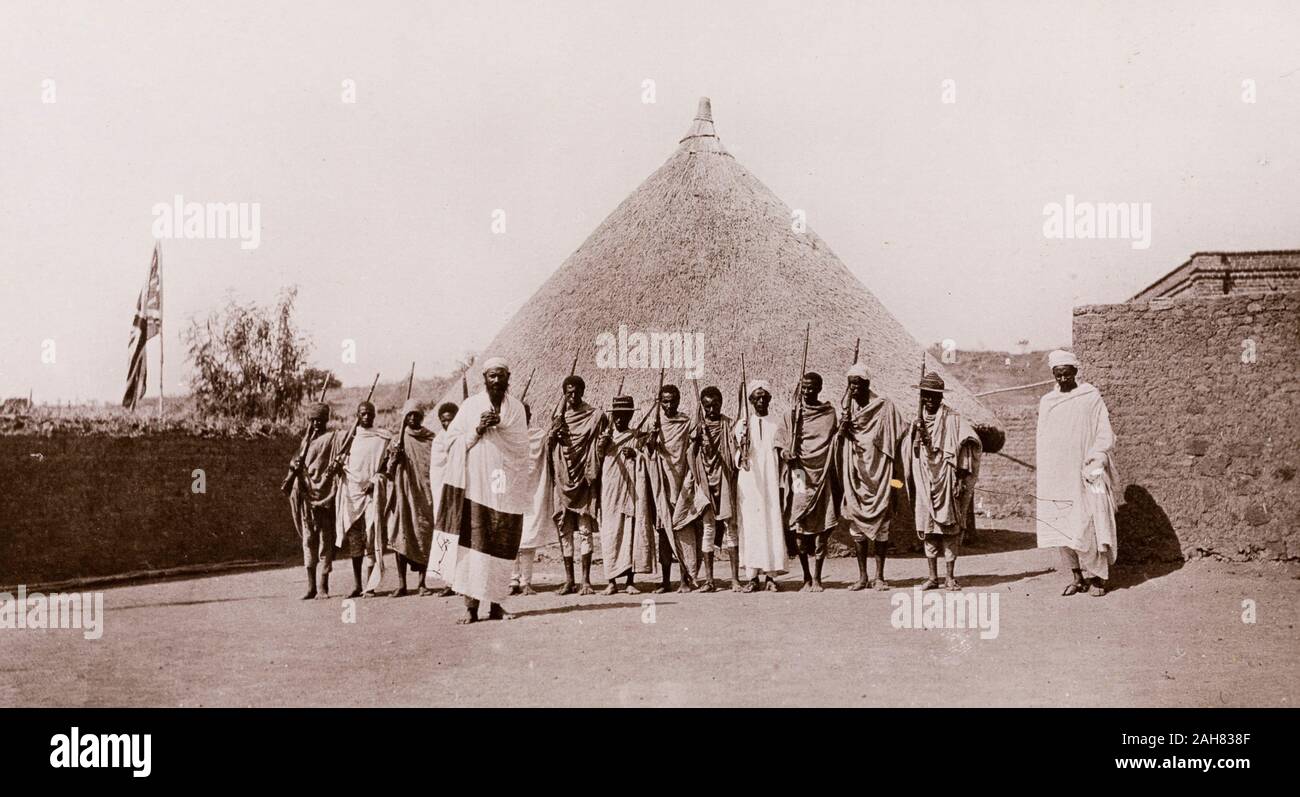 Sudan, stampato didascalia recita: "Gli Abissini a Gallabat. Pubblicato da G N Morhig, la farmacia inglese, Khartoum. Copyright 186'. Guardie armate al Sudan-Ethiopia borderA numero di armati uomini etiope sostare davanti a un round, capanna con il tetto di paglia a Gallabat, a guardia del confine tra il Sudan e l'Etiopia. Un union jack flag è sollevata su un pennone di sinistra della fotografia, [c.1906]. 2003/222/1/2/95. Foto Stock