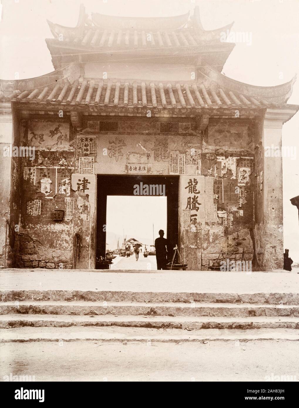 Hong KongChina, un gateway, decorata con una pagoda-tetto in stile, conduce al Porto di Kowloon. Semi-manifesti stracciati coperto con script cinesi rimangono incollati alla sua facciata. Manoscritto originale caption: Gateway a bordo di acqua Kowloon città vecchia Hong Kong, circa 1903. 1998/028/1/1/5. Foto Stock