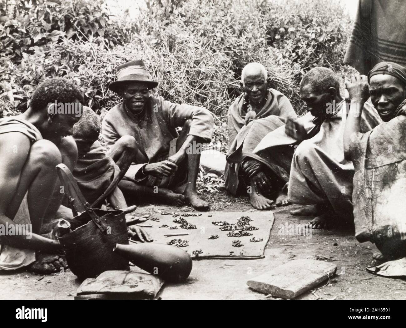 Kenya, un gruppo di uomini di kikuyu si riuniscono intorno a leggere le loro vicende da fagioli di dispersione a terra. Manoscritto originale caption: raccontare vicende di fagioli. S. Nyeri 1936, 1937. 1995/076/1/2/5/25. Foto Stock