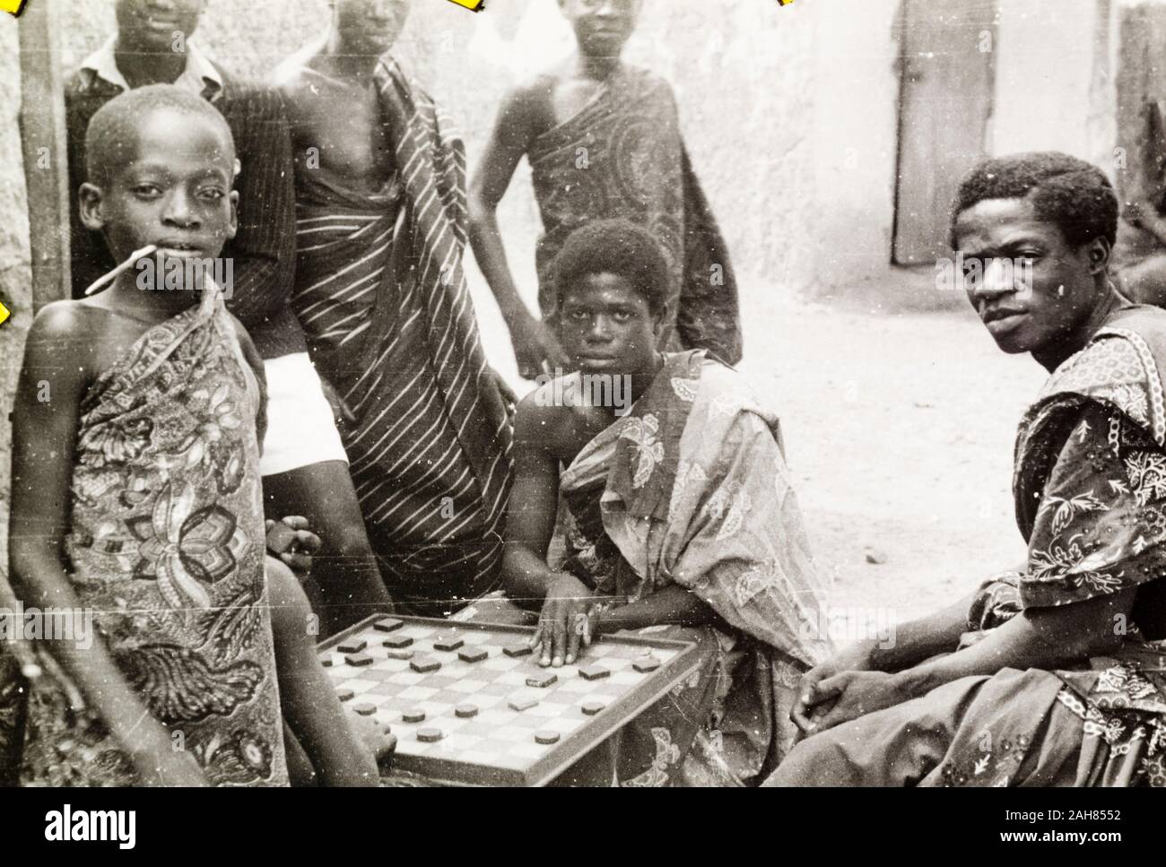 Oro CoastGhana, un gruppo di Asante (Ashanti) giovani si radunano per guardare due ragazzi giocare un gioco di bordo su un angolo di strada. Manoscritto originale didascalia: Ashanti giovani al tempo libero, 1951-52. 1995/076/5/2/2/64. Foto Stock