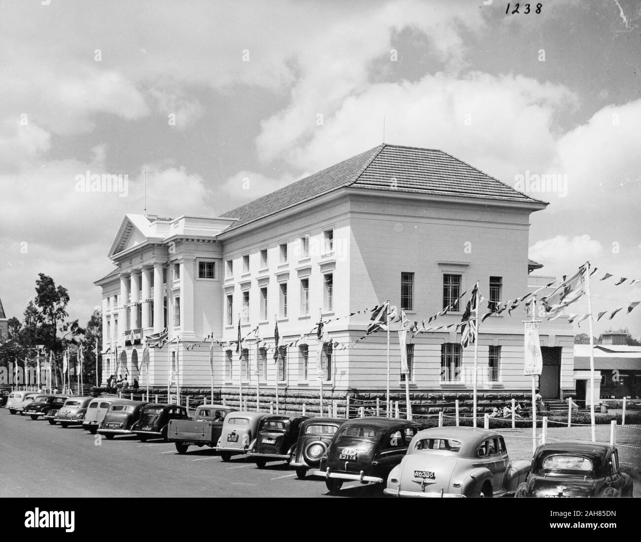 Kenya, elevazioni Frontale e Laterale di Nairobi municipio della città. Al di fuori dell'edificio sono una linea di bandiere recanti l Unione Jack insieme con bunting e bandierine raffigurante uno struzzo con le parole "CITTÀ DI NAIROBI.'' Una bandiera porta la croce di Sant'Andrea. Operai può essere visto di erigere una bandiera nella parte anteriore del Municipio e linea di auto la strada fuori, febbraio 1952. 2001/090/1/4/1/58. Foto Stock