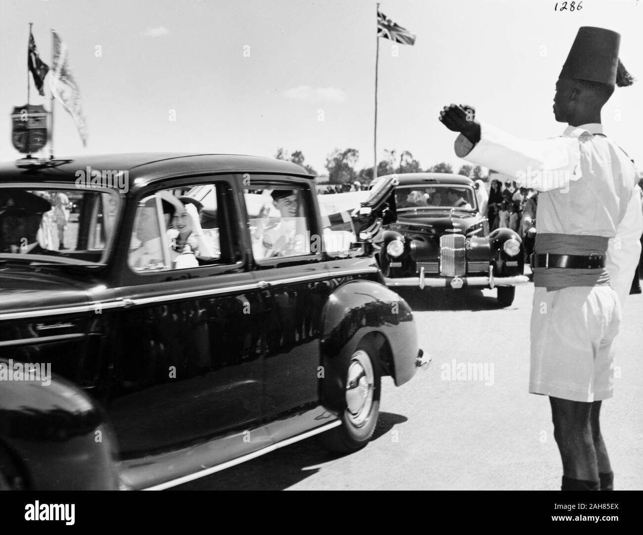 Il Kenya, la Principessa Elisabetta e il Duca di Edimburgo in auto da Eastleigh Airport in una macchina che porta le insegne regali. Dietro questa macchina aziona un'altra auto anche il cuscinetto del Royal Crest. Un africano funzionario di polizia punti nella direzione di marcia, febbraio 1952. 2001/090/1/4/1/16. Foto Stock