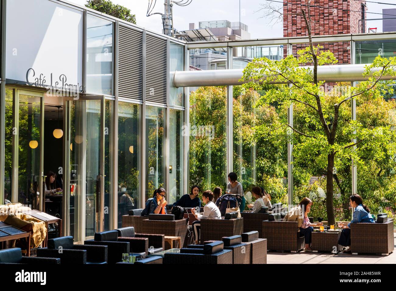 La gente seduta al di fuori del cate Le Pommier, a tavoli e sedie in un cortile di vetro in giapponese Associazione infermieristica Edificio Omotesando, Tokyo. Foto Stock