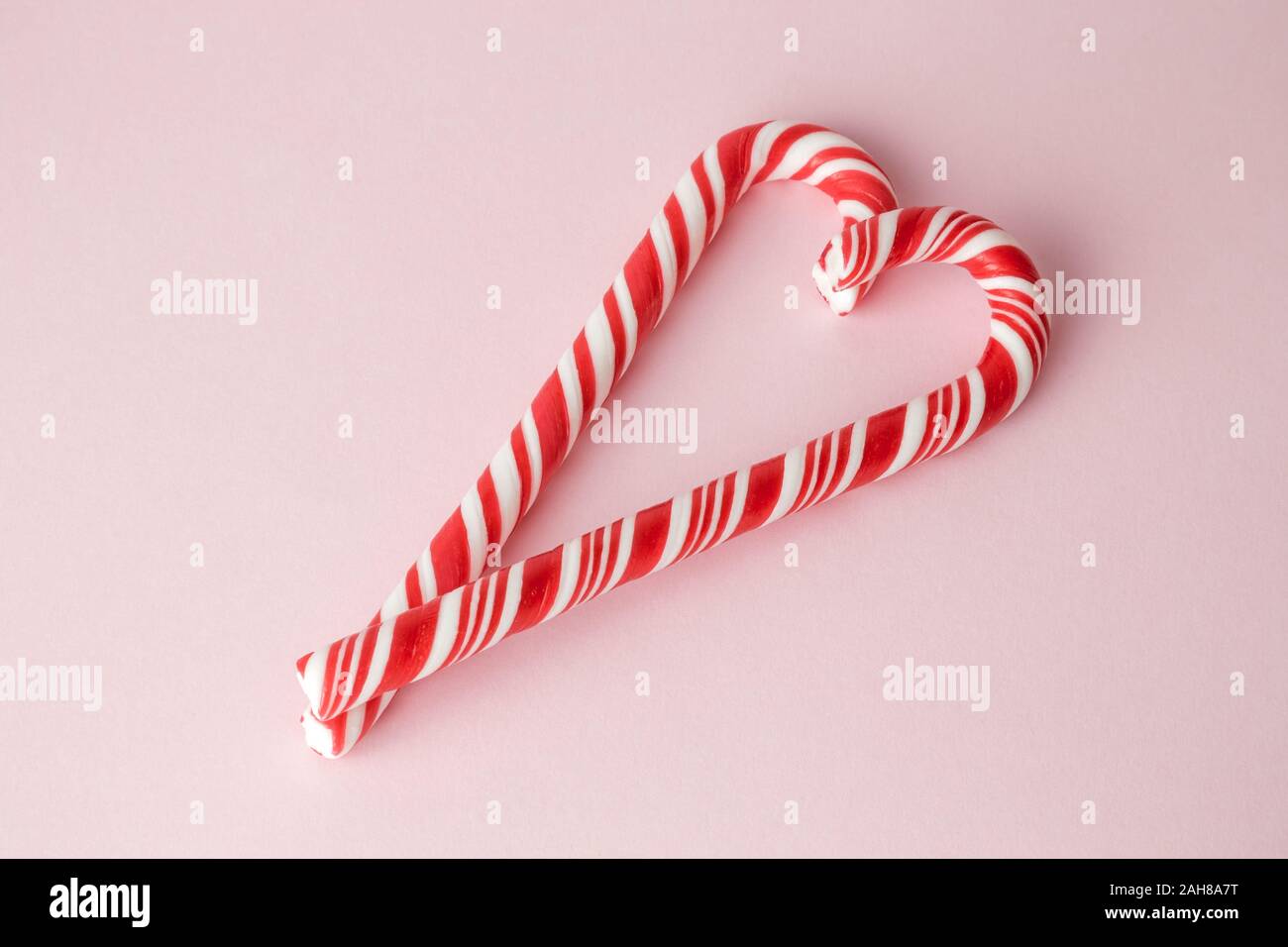 Due canne di caramella a forma di cuore sul rosa pastello background creativo minima Natale o Capodanno concetto. Spazio per la copia. Foto Stock