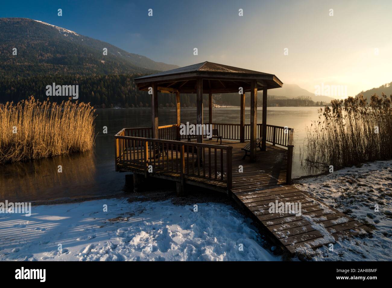 Ampia vista panoramica sul paesaggio invernale italiano settentrionale, con gazebo in legno sul lungomare circondato da un canneto e da una montagna lontana Foto Stock