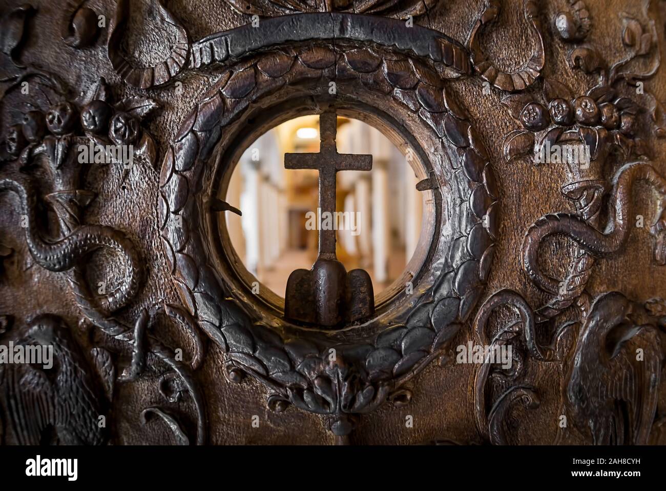 Un primo piano simmetrico di un'antica porta intarsiata in legno con apertura circolare e croce cristiana al centro Foto Stock
