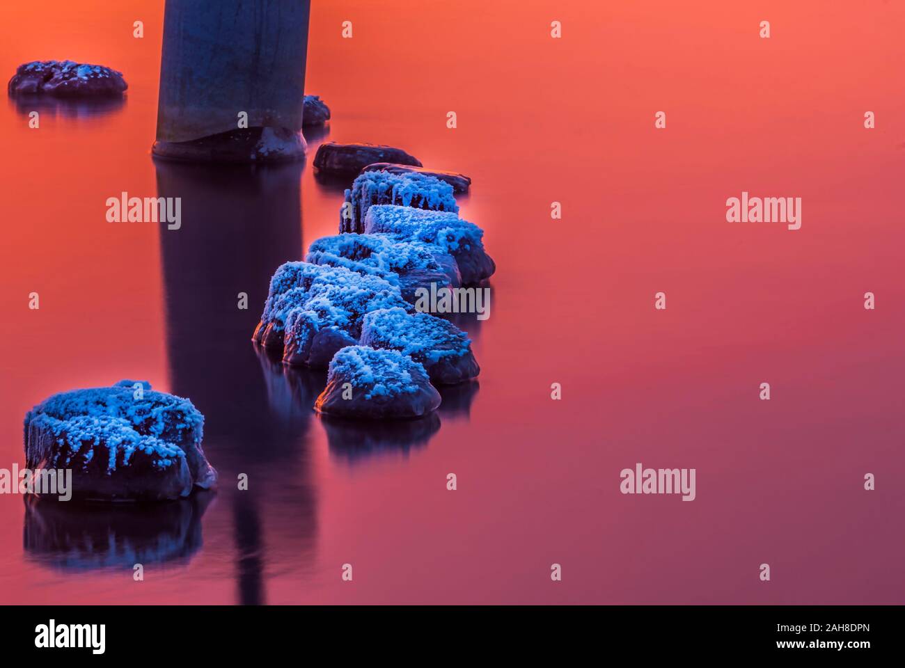 La coperta di neve rocce in acqua calma sotto il tramonto mozzafiato Foto Stock