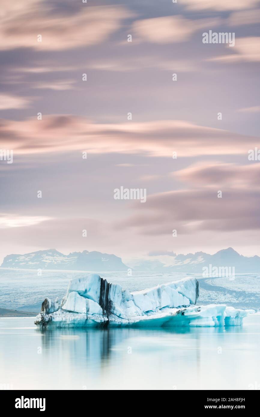 Iconico paesaggio islandese al tramonto, con un iceberg azzurro a righe che galleggia in primo piano, un ghiacciaio sullo sfondo, sotto un cielo lilla Foto Stock