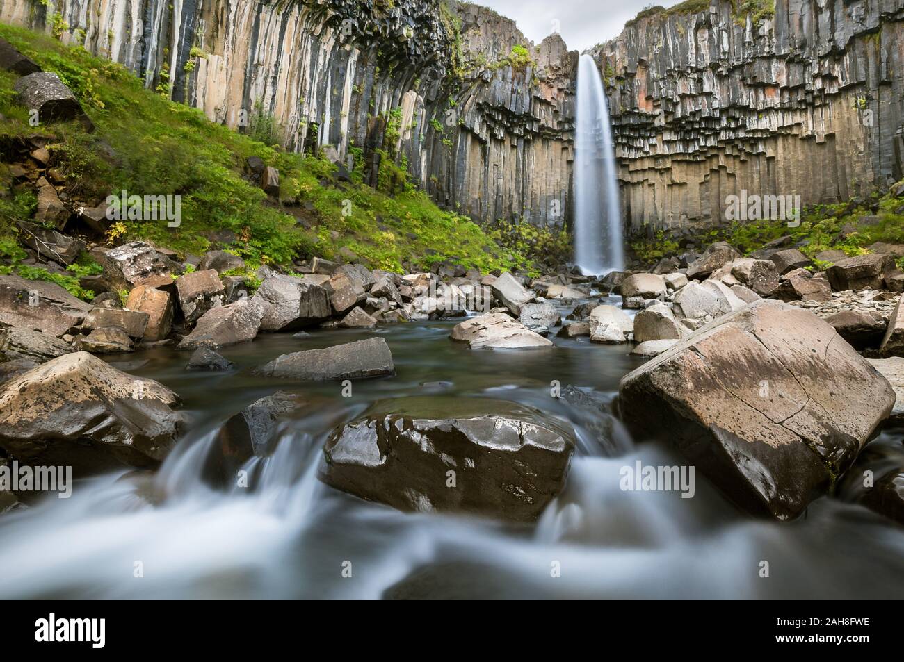 Esposizione a lungo e basso angolo dell'iconica cascata islandese di Svartifoss, con la sua acqua che scorre tra ciottoli e rocce ricoperte di muschio Foto Stock