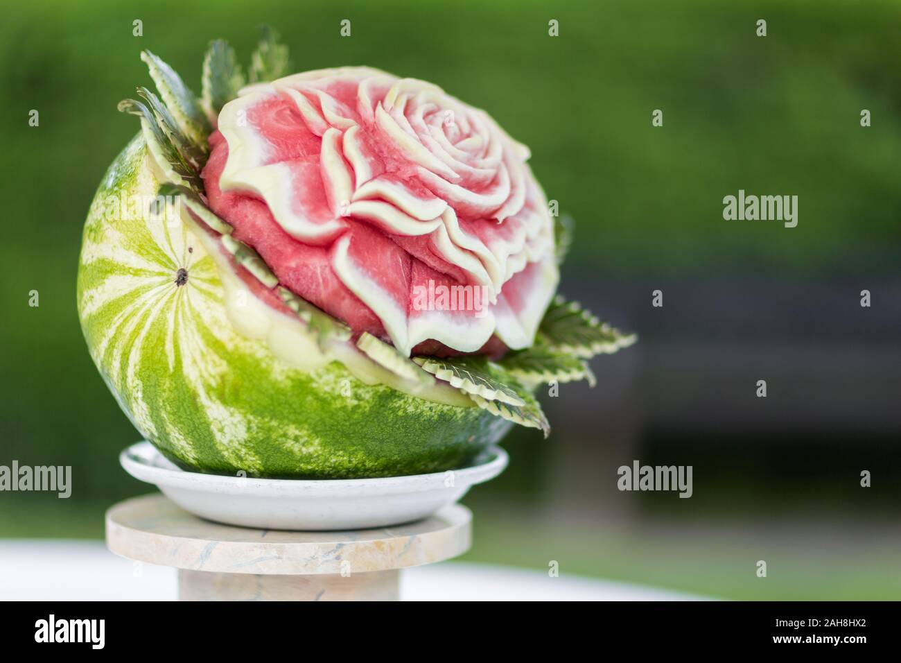 Primo piano di un cocomero scolpito per assomigliare ad un fiore in fiore, contro uno sfondo verde bokeh Foto Stock