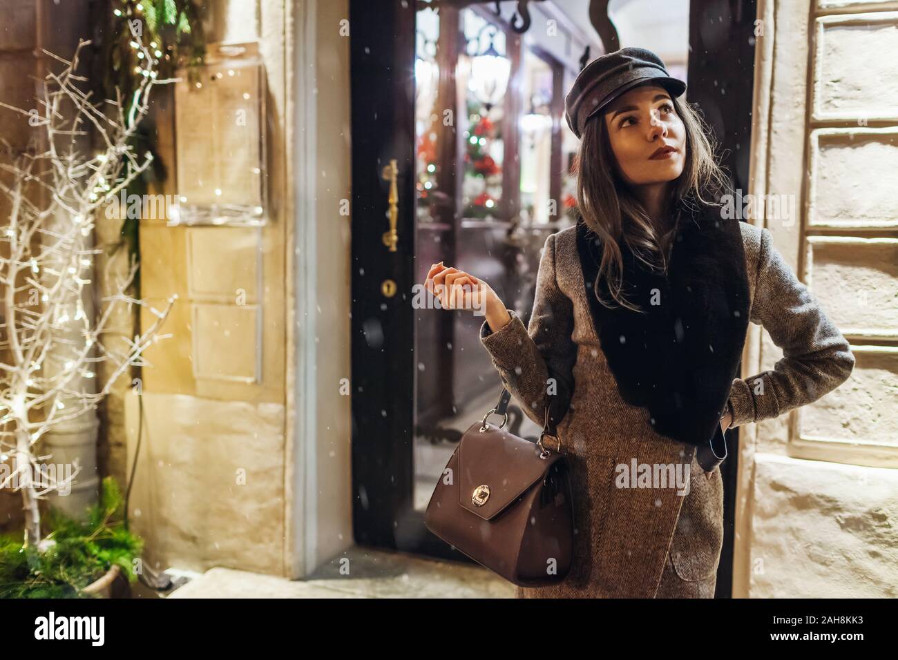 Inverno moda. Natale e Anno Nuovo concetto. La donna in attesa amici su una strada di città da holiday decorato cafe vetrine. Foto Stock