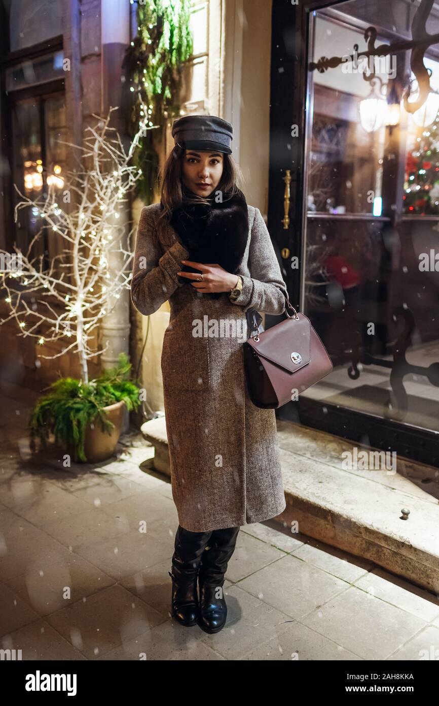 Inverno moda. Natale e Anno Nuovo concetto. La donna in attesa amici su una strada di città da holiday decorato cafe vetrine. Foto Stock