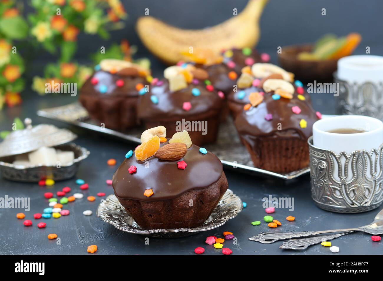 Banana-muffin al cioccolato, ricoperti di una glassa e confetteria confetti sono situati su uno sfondo scuro Foto Stock