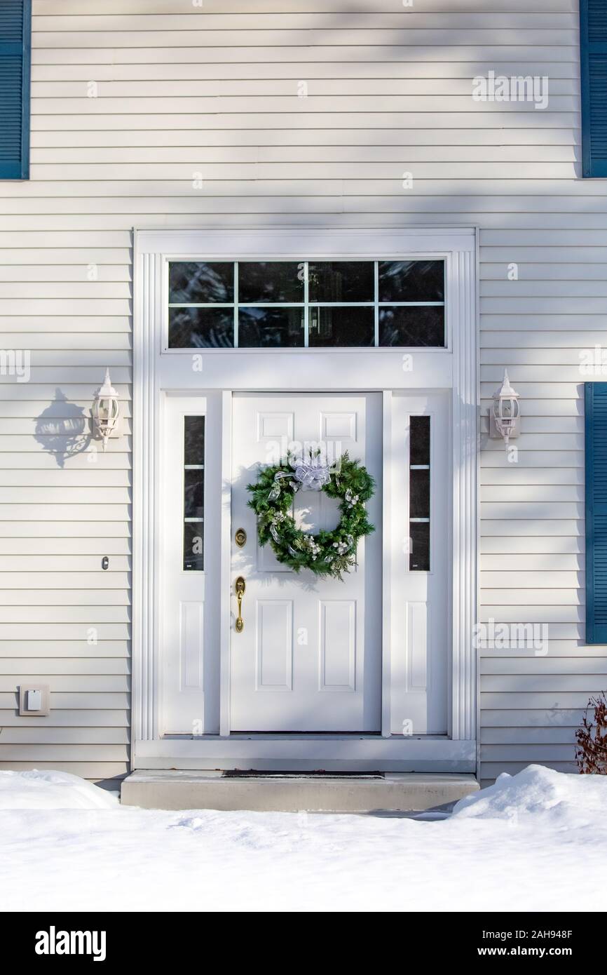 La parte anteriore della casa bianca con una ghirlanda di Natale sulla porta anteriore in inverno poco prima di Natale in verticale Foto Stock