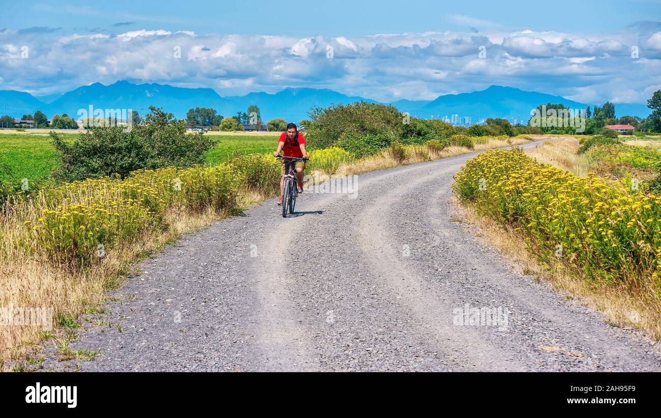Delta, B.C., Canada - 20 luglio, 2019. Un giovane corse in mountain bike senza un casco, su una strada di ghiaia in un ambiente rurale vicino a Vancouver. Foto Stock