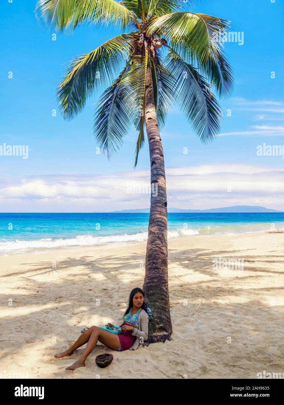 Mindoro Island, Filippine - Febbraio 16, 2011. Una giovane donna asiatica si siede sotto un albero di palme sulla spiaggia. Foto Stock