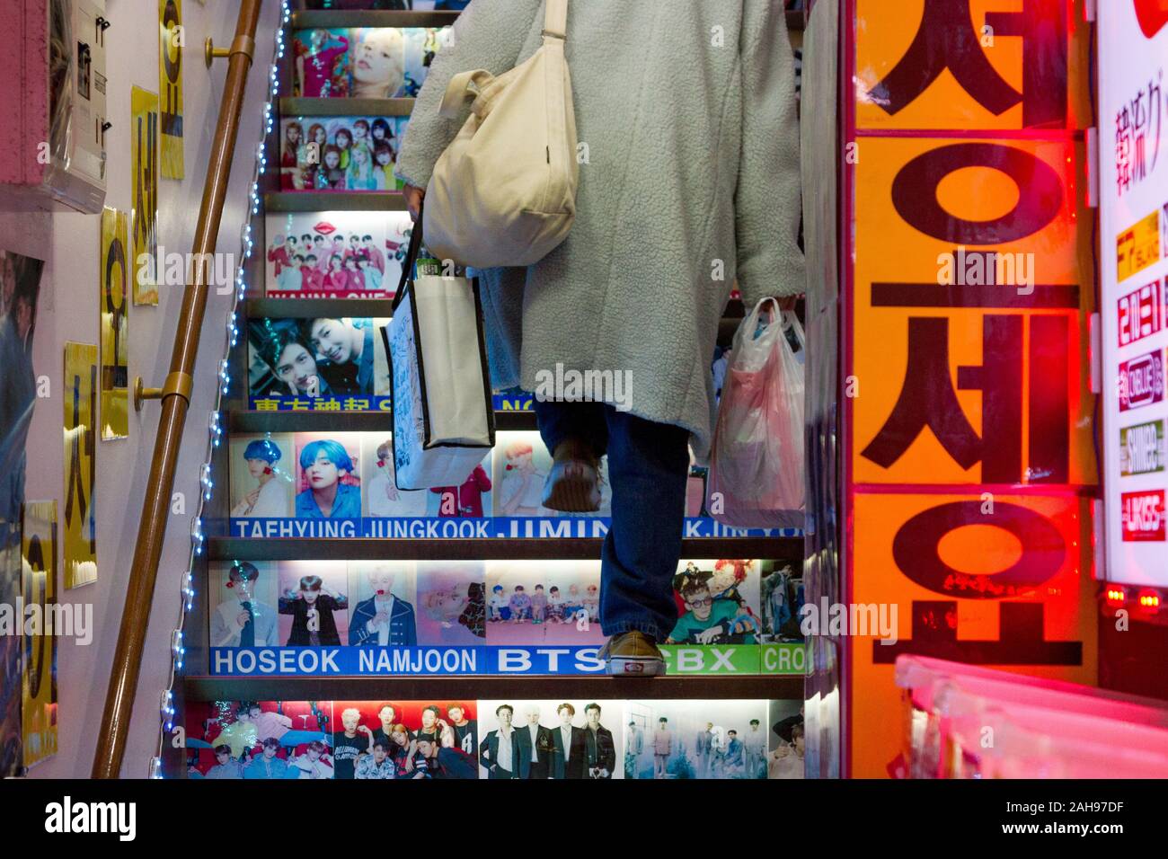 Una donna il trasporto delle borse della spesa salite le scale con immagini di idoli coreano e celebrità su di essi in un negozio di Shin-Okubo, Shinjuku, Tokyo, Giappone. Foto Stock