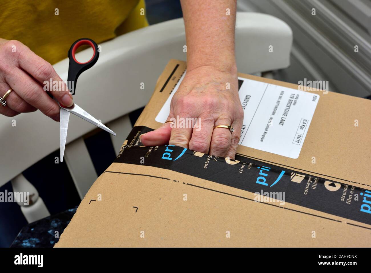 Donna con le mani in mano con le forbici per aprire un Amazon la consegna di pacchi Foto Stock