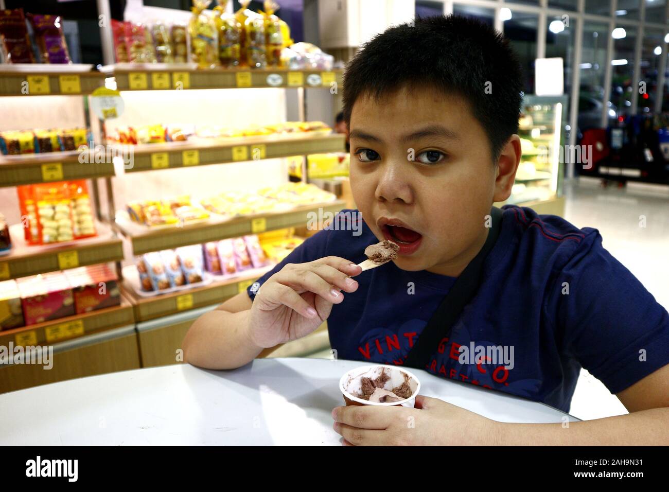 Antipolo City, Filippine - 21 dicembre 2019: il giovane ragazzo filippino mangia il gelato in un bicchiere mentre all'interno di un supermercato. Foto Stock