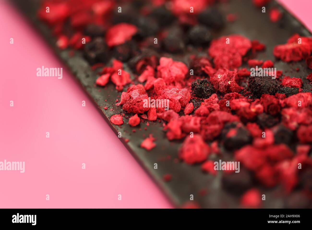 Dark a basso contenuto calorico il cioccolato con secchi di bacche rosse sul rosa chiaro sfondo, il fuoco selettivo Foto Stock