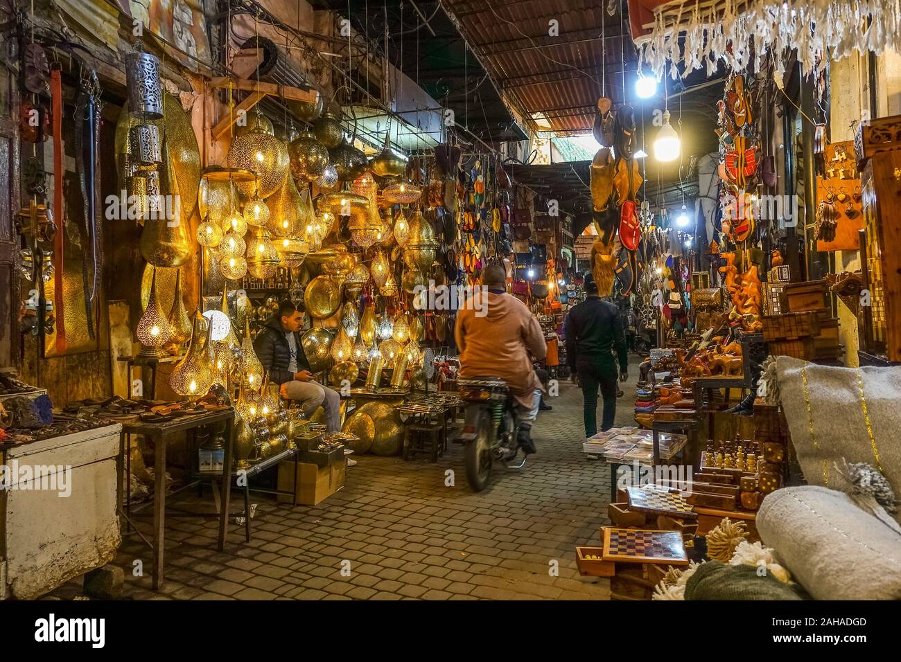 Uomo con gli scooter aziona attraverso souk di Marrakech, lanterne e lampade, la lavorazione del rame si spegne nel Souk, Medina, Marrakech, Marocco. Foto Stock