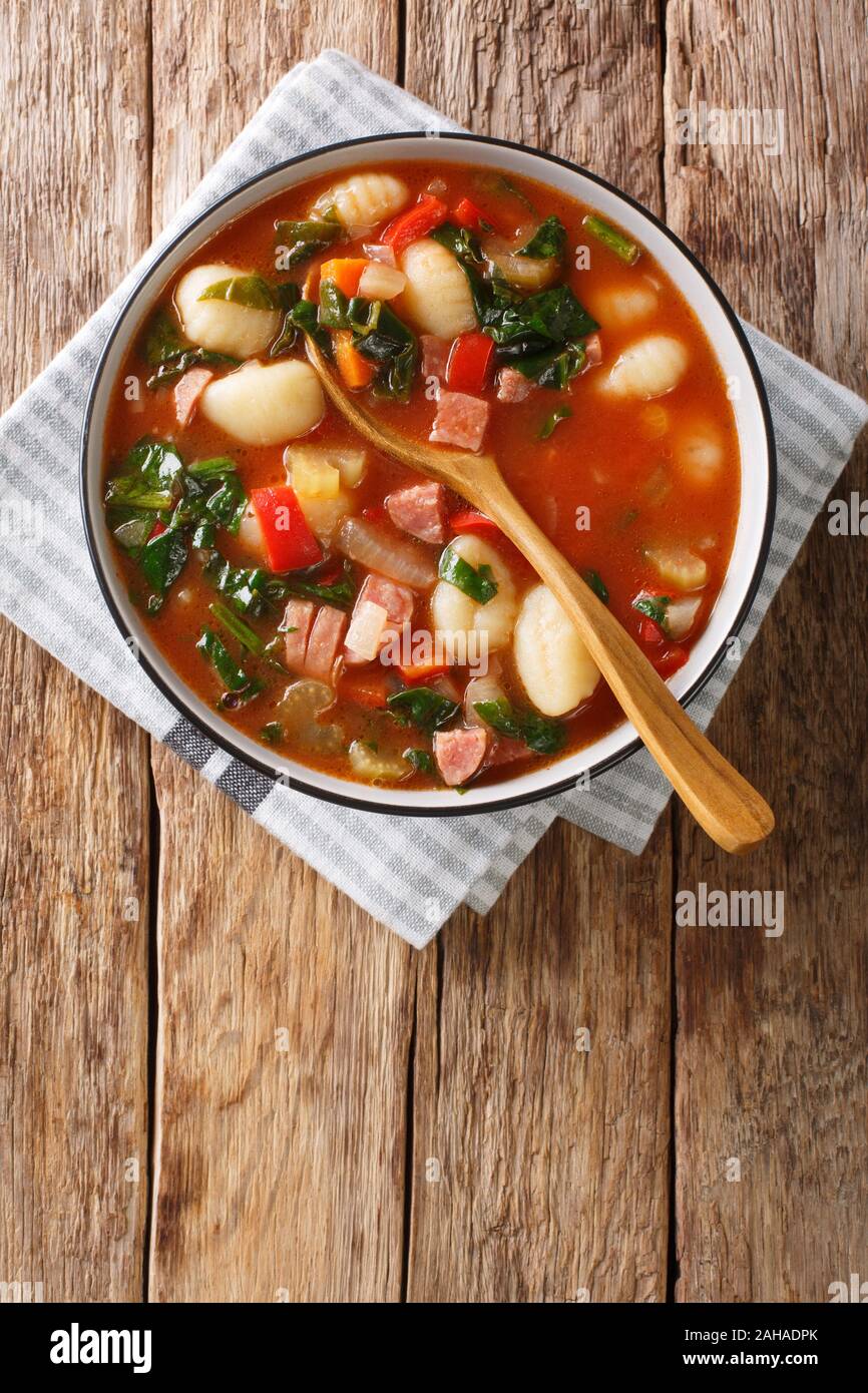 Piccante zuppa di pomodoro con gnocchi, salsicce, spinaci e verdura close-up in una ciotola sul tavolo. Verticale in alto vista da sopra Foto Stock