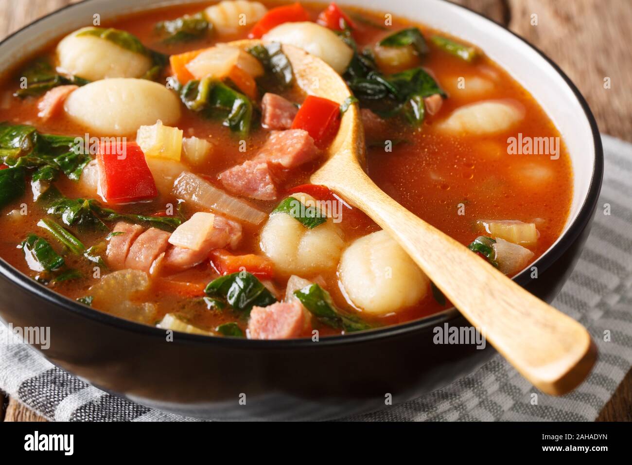 Piccante zuppa di pomodoro con gnocchi, salsicce, spinaci e verdura close-up in una ciotola sul piano verticale. Foto Stock