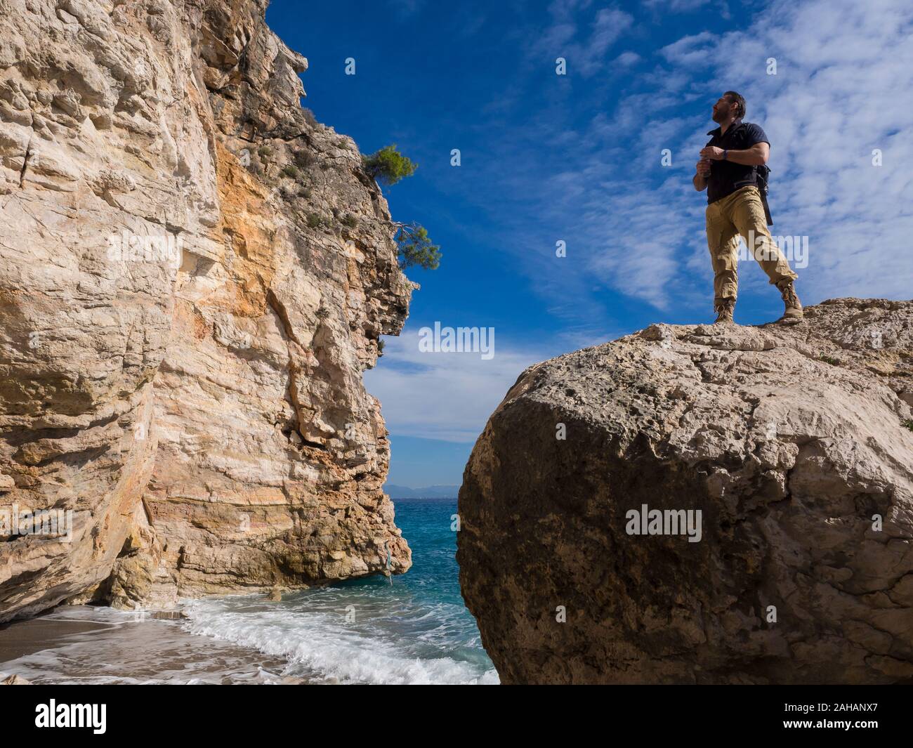 Viaggiatore con zaino sulle rocce vicino al mare che guarda lontano. Estate Vacanze di viaggio. Bel giovane turista caucasica uomo in abiti casual all'aperto Foto Stock