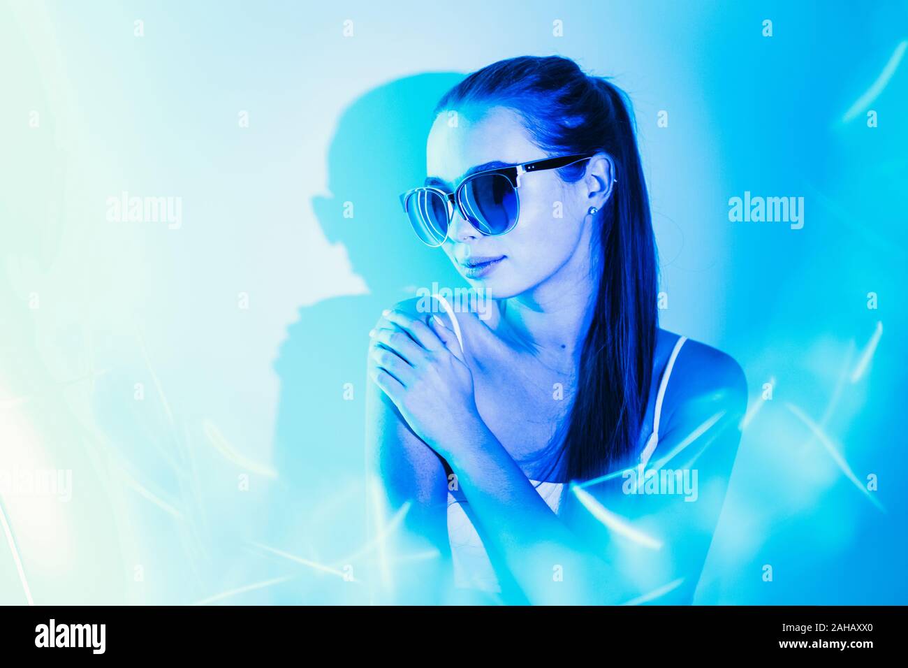 Notte ritratto di una giovane ragazza attraente con la riflessione in occhiali da sole in neon blu lampeggia. Copia dello spazio. Foto Stock