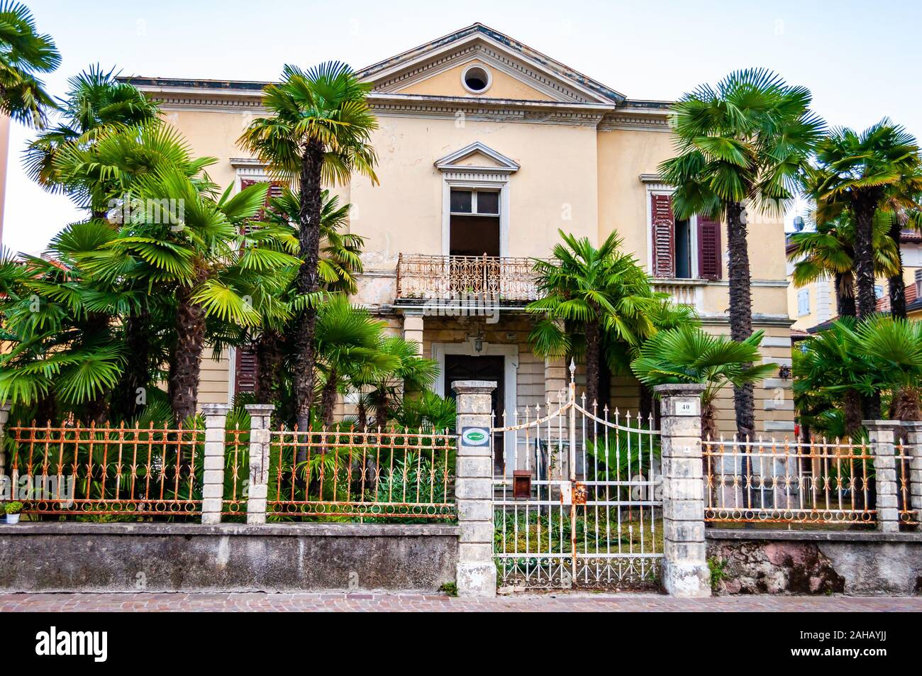 Abbandonato due piani classica casa italiana con crescente palm nel giardino recinto metallico e la porta d'ingresso a Riva del Garda, Lombardia, Italia Foto Stock