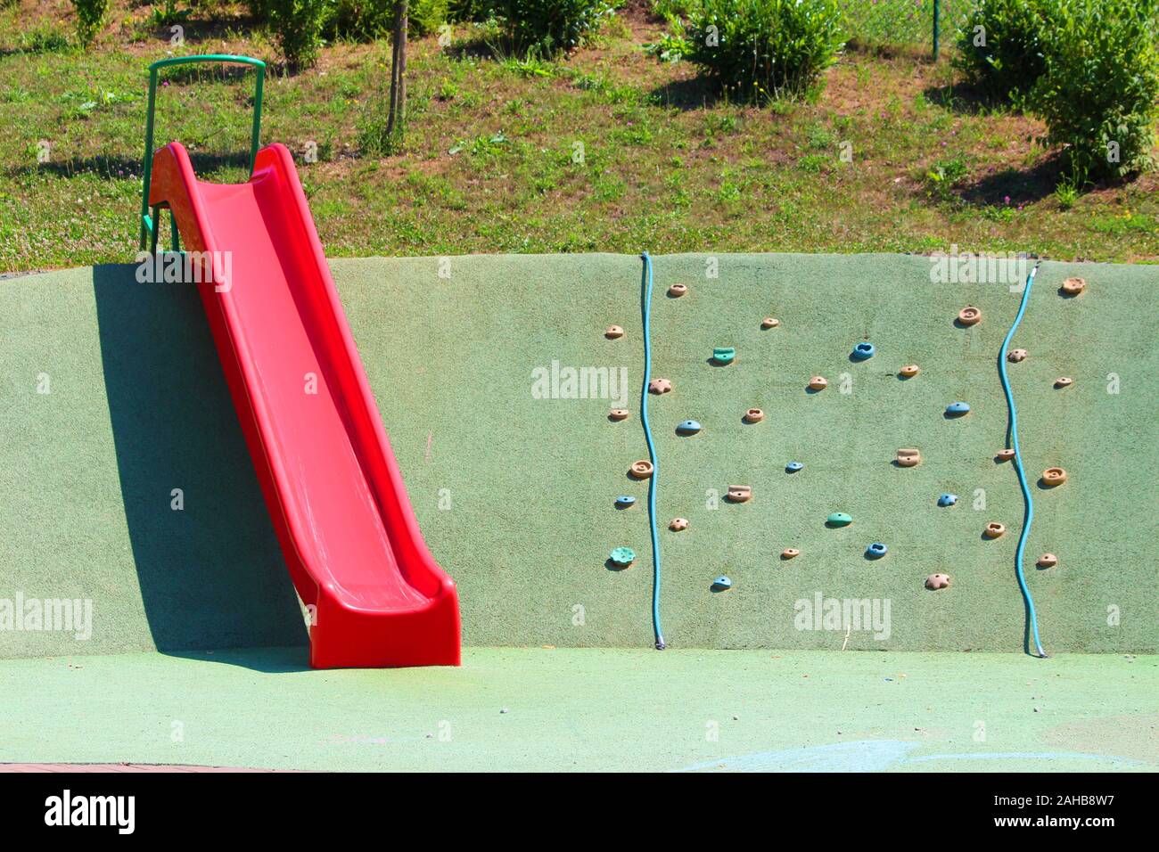 Rosso in plastica scorrono accanto a bambini parete di arrampicata a livello locale parco giochi con parete di arrampicata detiene in varie forme e colori miscelati con funi di arrampicata Foto Stock