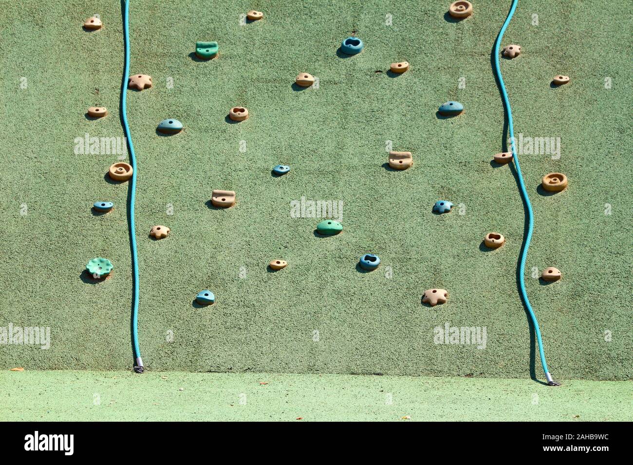 Bambini piccoli parete di arrampicata a livello locale parco giochi con parete di arrampicata detiene in varie forme e colori miscelati con arrampicarsi sulle funi circondato da verdi Foto Stock