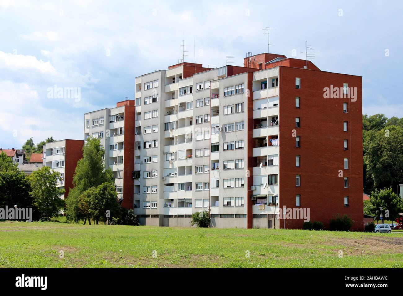 Condominio bianco con red building block di fianchi e più balconi, circondato da erba e alberi di alto fusto su nuvoloso cielo blu sullo sfondo Foto Stock