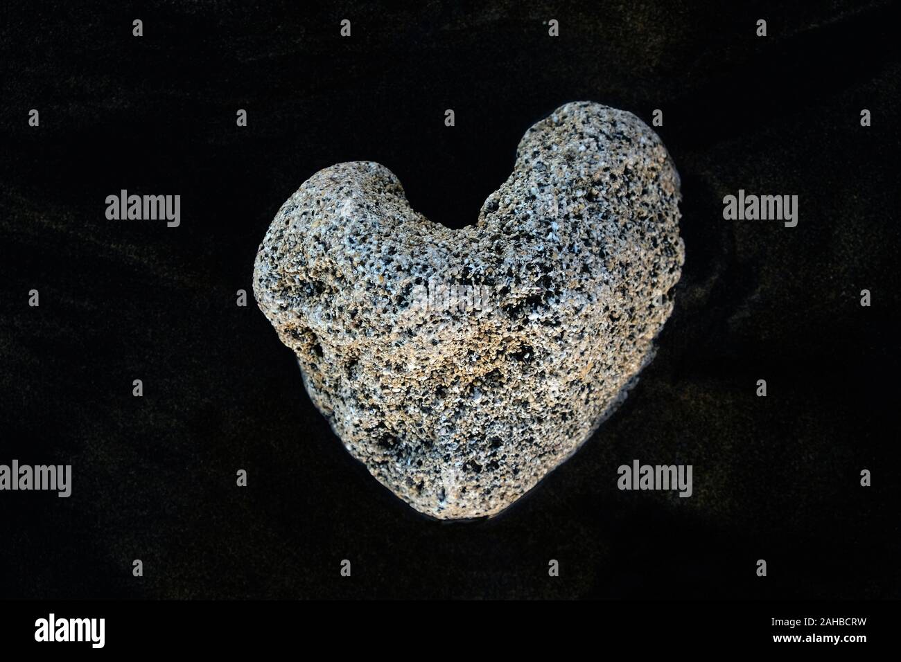 Bianco a forma di cuore sulla pietra di sabbia nera vulcanica. Foto Stock