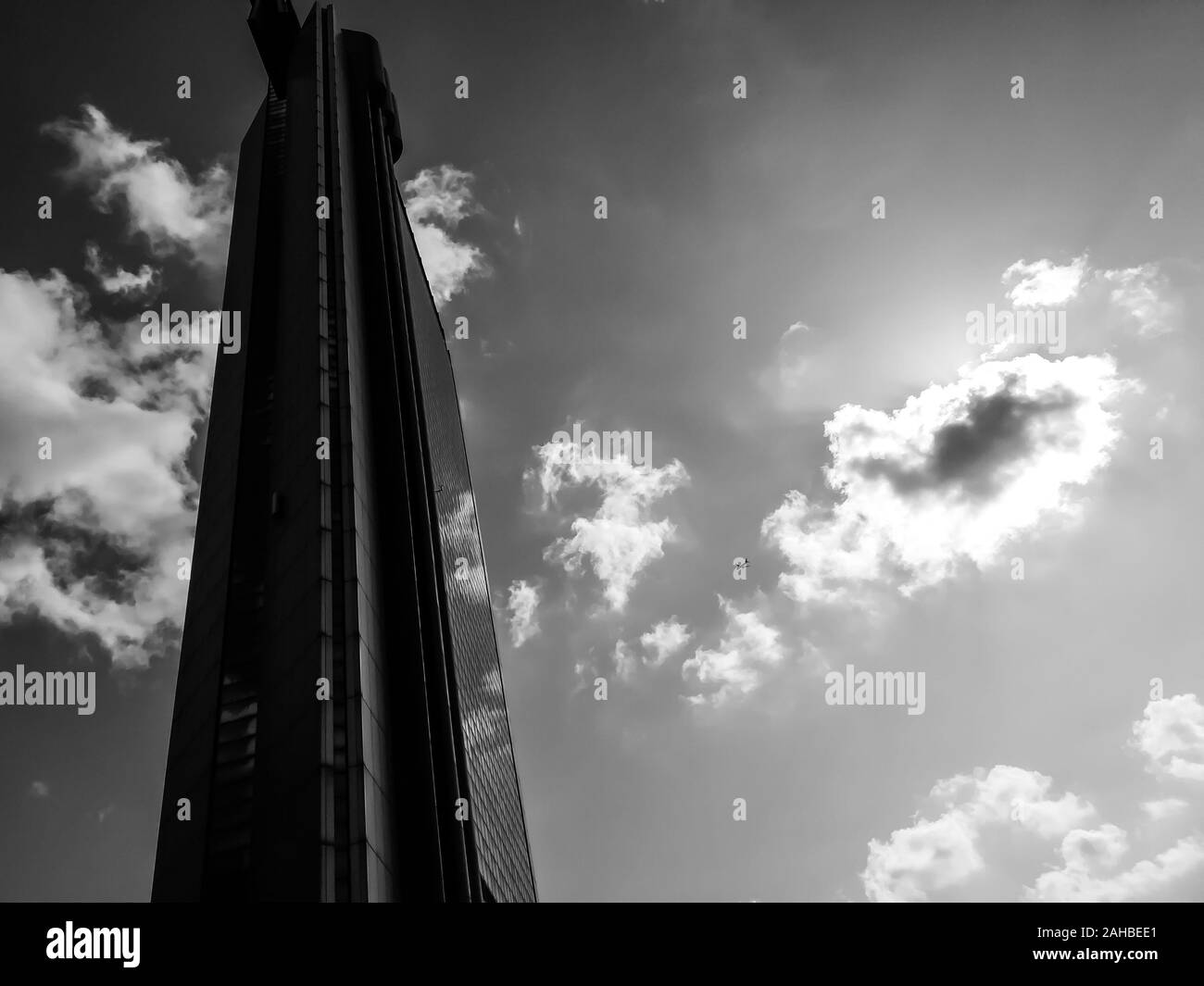Foto in bianco e nero di un singolo grattacielo con un piccolo aereo che vola vicino ad esso. Scena artistica urbana. Foto Stock
