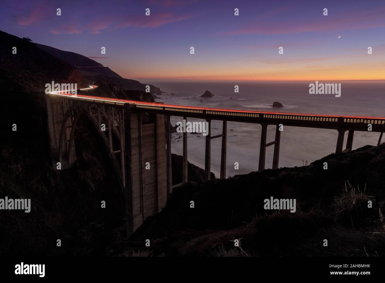 Auto sentieri di luce illuminando Bixby ponte su un inverno al tramonto Foto Stock
