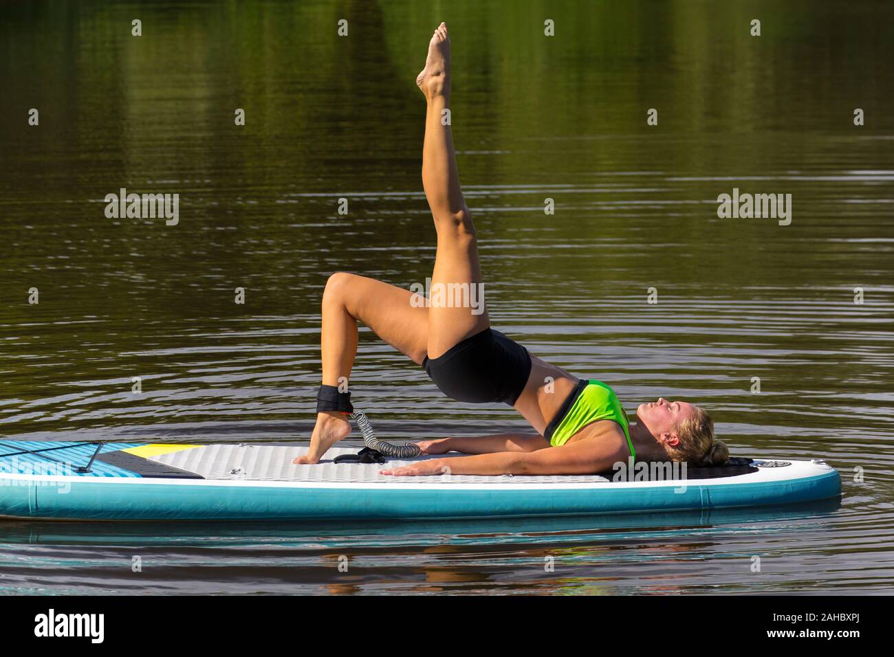Giovane donna caucasica in postura yoga con la gamba in alto sulla scheda pala Foto Stock