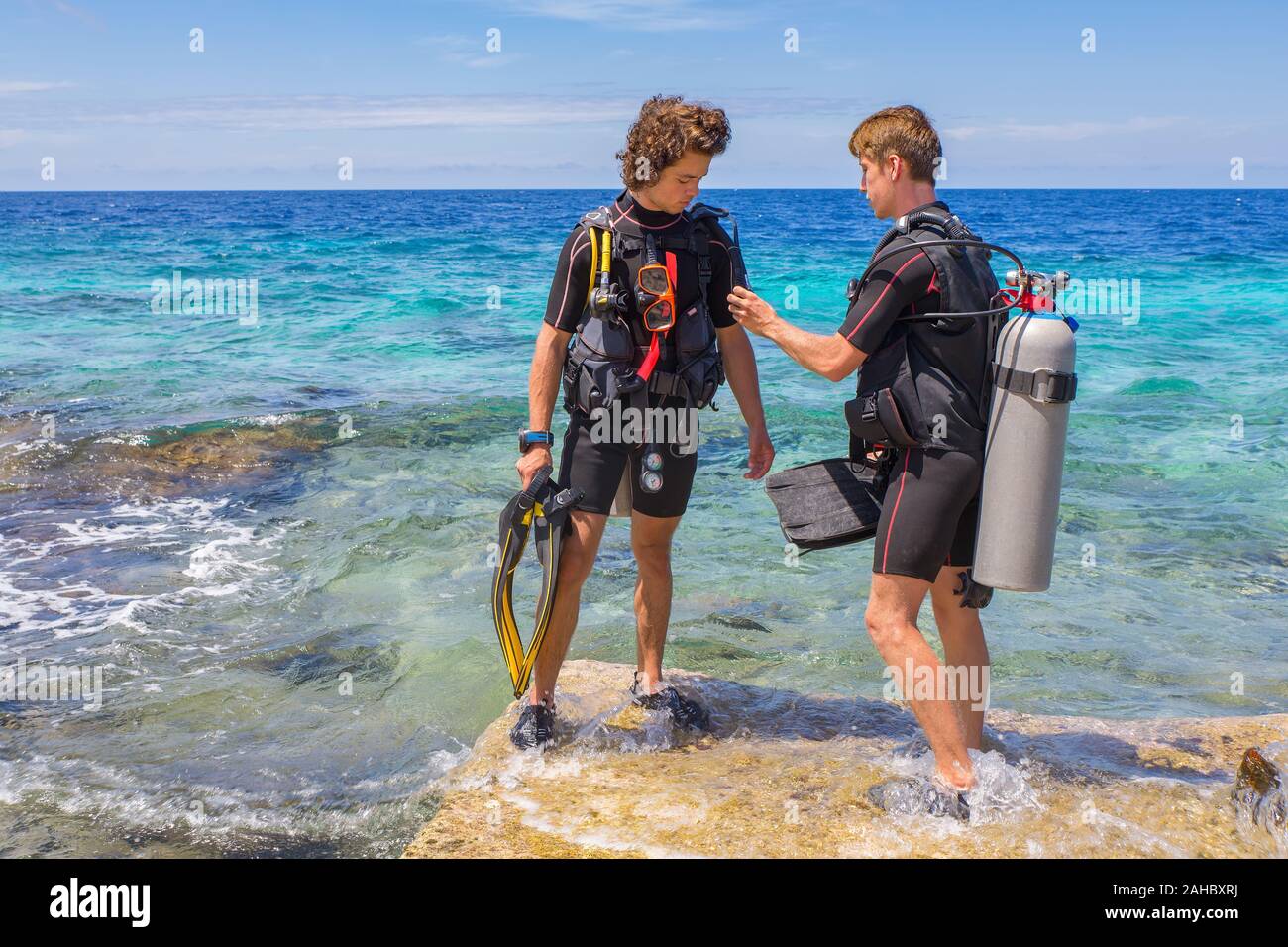 Due giovani tuffatori controllando la loro attrezzatura per immersioni nel mare di Bonaire Foto Stock
