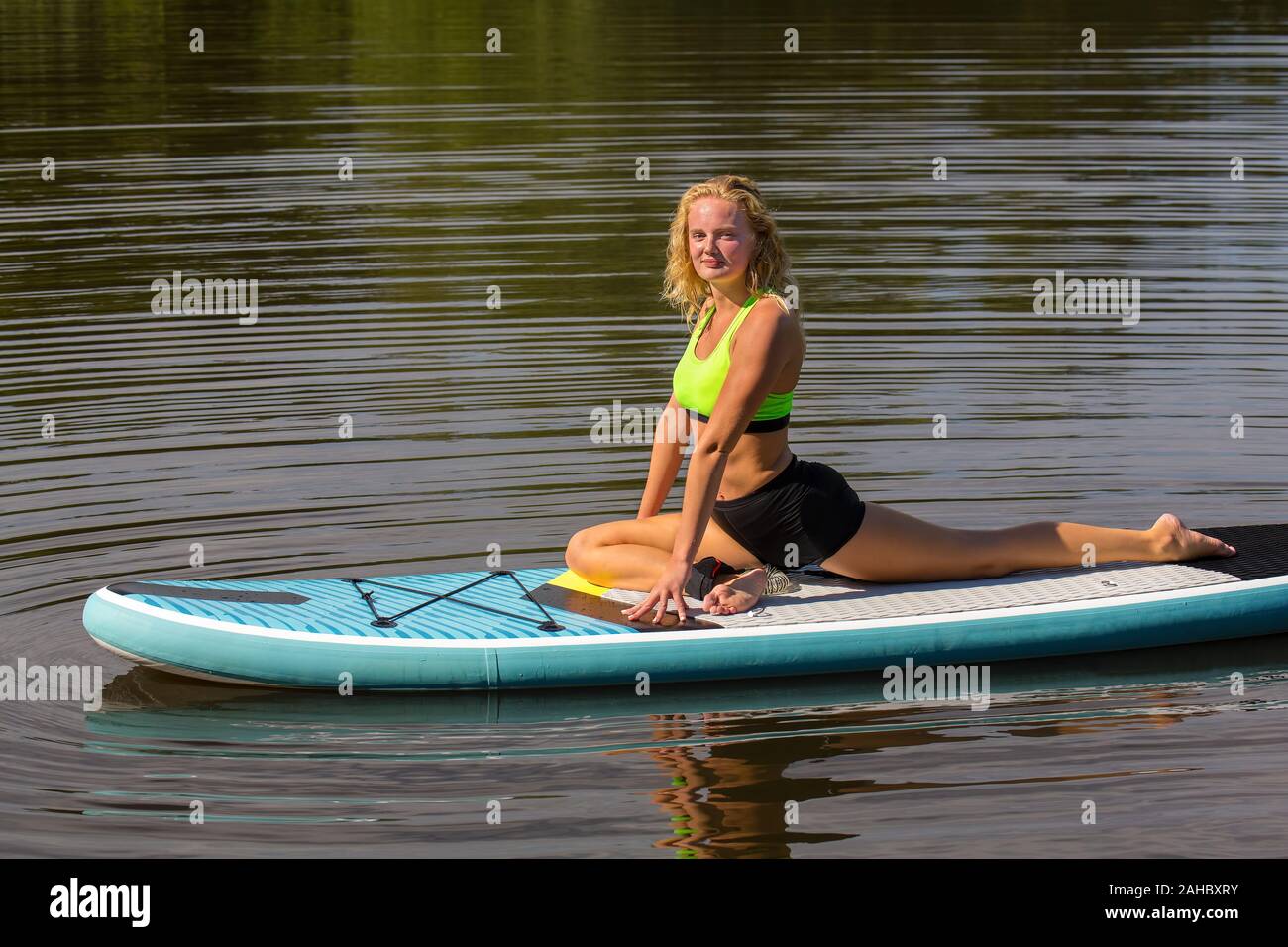 Giovane donna caucasica yoga in Swan posizione sulla scheda di racchetta in acqua Foto Stock