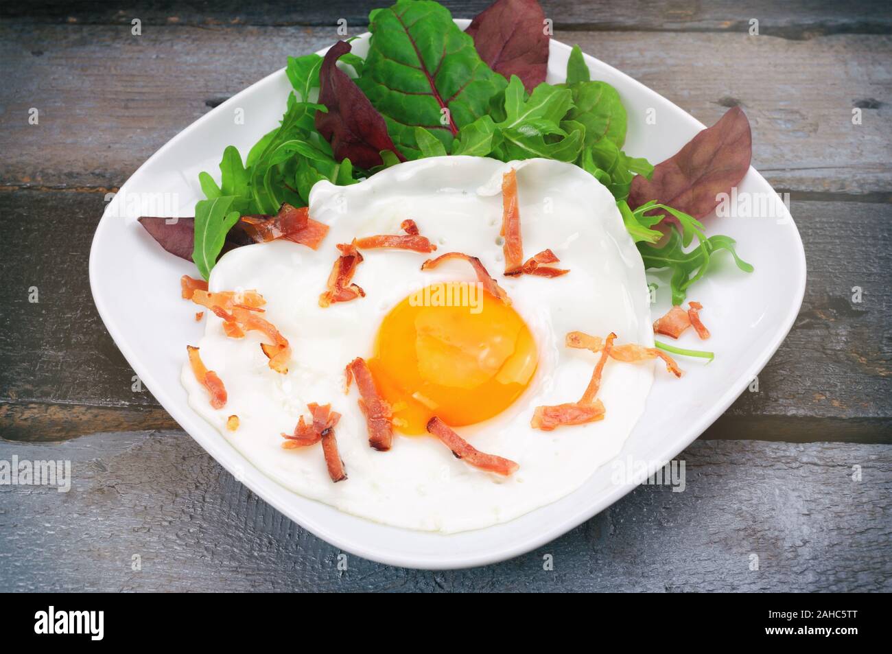 Uova fritte con pancetta e insalata mista su tavola in legno Foto Stock