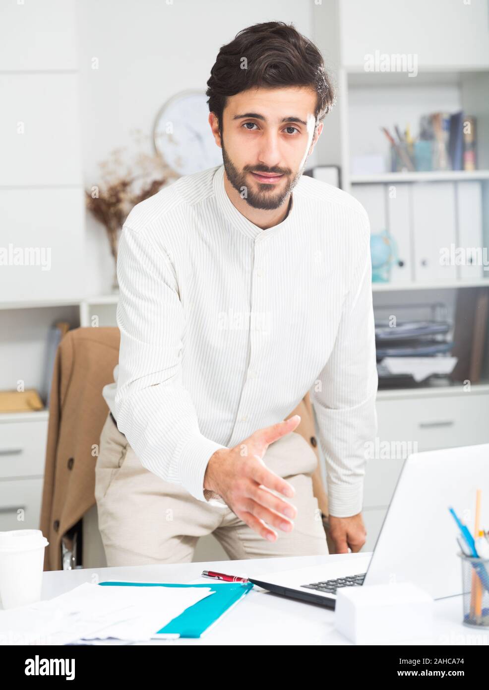 Amichevole maschio giovane lavoratore di ufficio con la mano estesa per stretta di mano in ufficio Foto Stock
