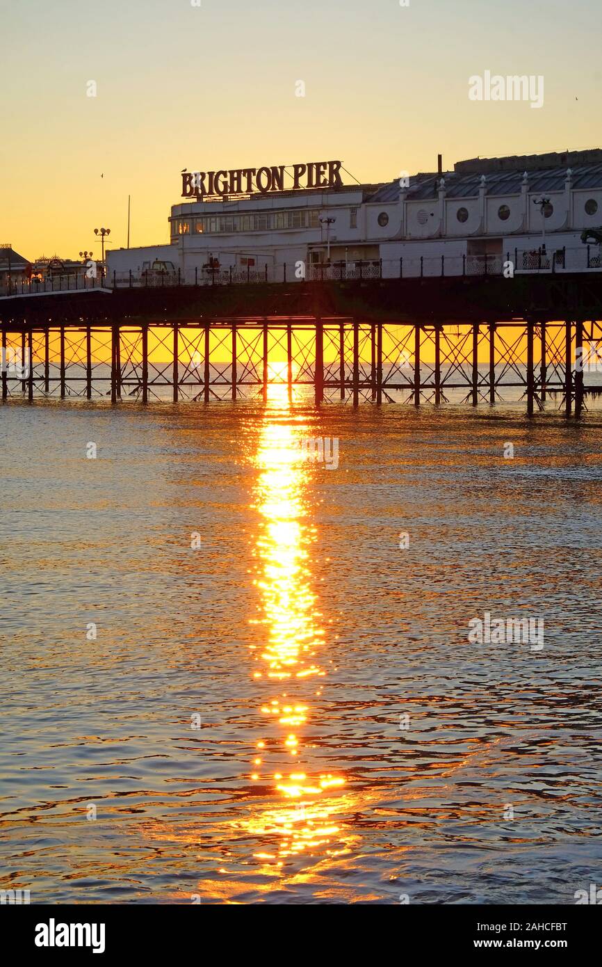 Il Brighton Pier, la parte anteriore del molo con il nome su di esso, guardando dal mare, il sole tramonta sotto il molo formando una bella stella effetto raffica di Foto Stock
