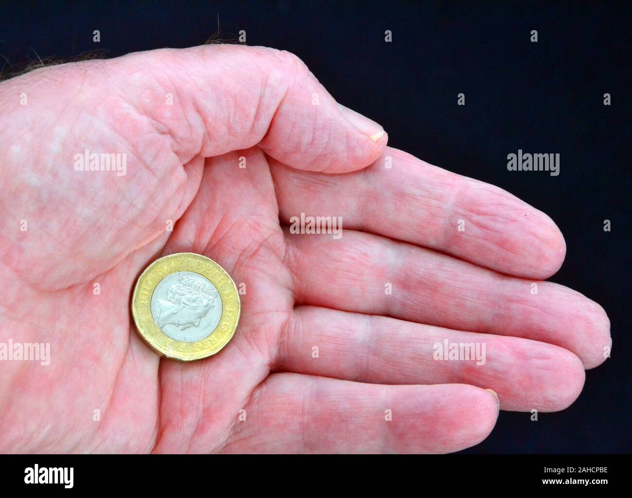 Uno britannico pound coin nel palmo di una mano di un uomo contro uno sfondo scuro Foto Stock