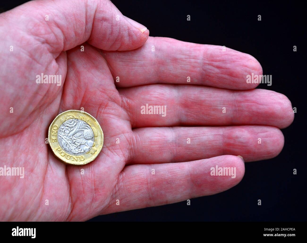 Uno britannico pound coin nel palmo di una mano di un uomo contro uno sfondo scuro Foto Stock