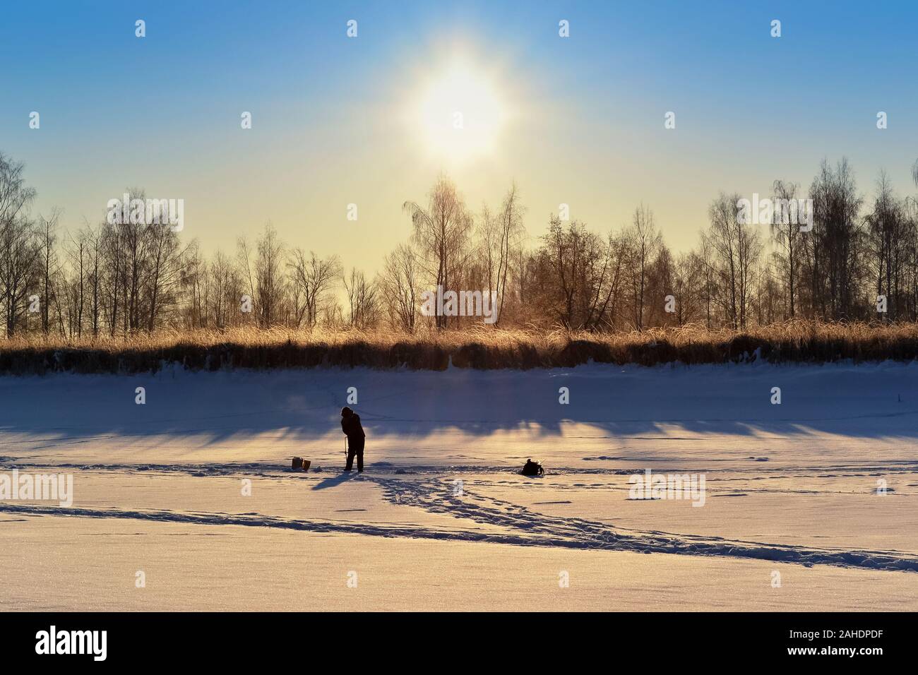 Silhouette di un pescatore solitario su una coperta di neve sul fiume, alla luce del sole che sorge Foto Stock