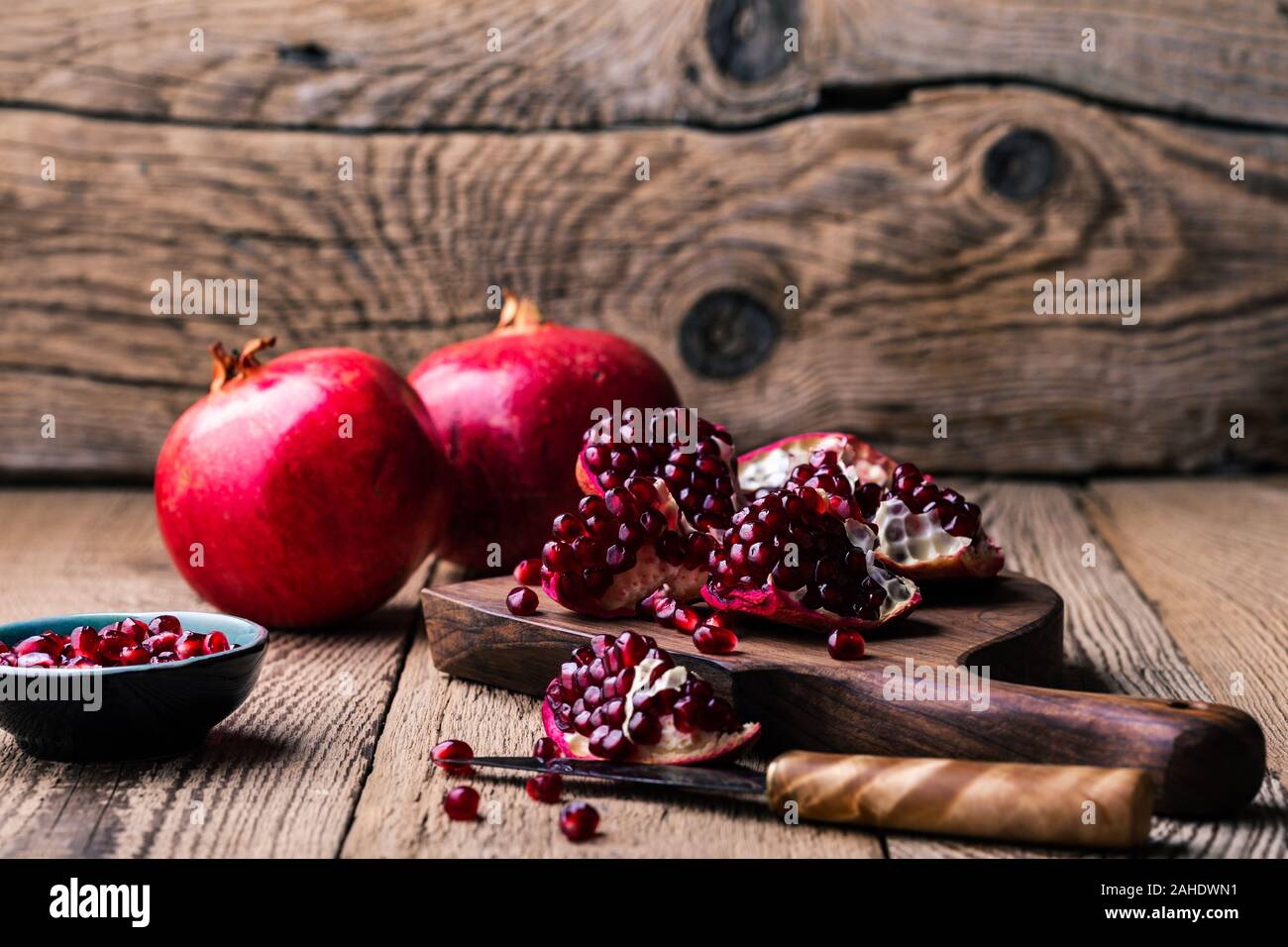 Fresche e mature melograni intero, aperto il melograno e semi in ciotola, coltello sulla tavola di legno, still life, close up Foto Stock