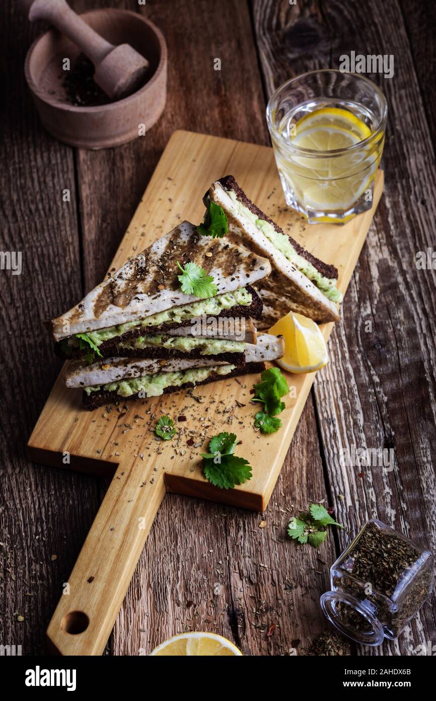 La colazione o il brunch, avocado pane di segale brinda con grigliate di erborinati tofu, impianto basato snack serviti rustico di legno, sano pasto vegano Foto Stock