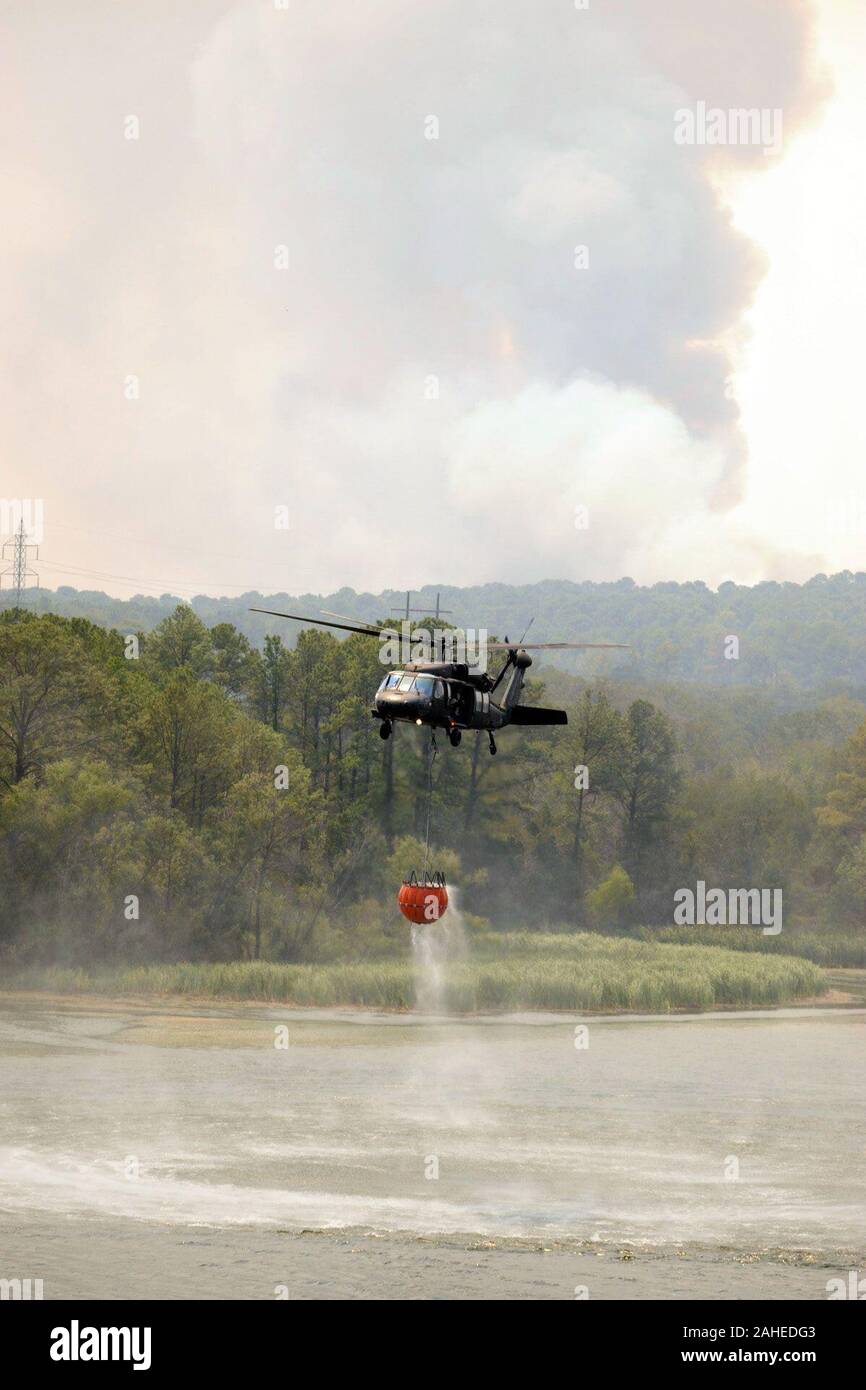 Un Texas National Guard UH-60 Black Hawk capi torna alla battaglia di Blaze in background dopo essere stato ricariche alla sua antenna di erogazione di acqua in prossimità della benna Bastrop Texas, Sett. 6, 2011. Texas National Guard per equipaggi lanciato al di fuori dell'esercito di Austin Aviation Facility per la lotta contro gli incendi selvaggi. Essi sono parte di un interagenzie di risposta che include U.S. Dipartimento dell'Agricoltura, Servizio di Foresta che quando è necessario volare missioni di osservazione per antenna diretta wildfire operazioni di combattimento. Dal 1975, il Dipartimento di Agricoltura e il ministero degli Interni hanno avuto un accordo tra le agenzie con il Dipartimento di Def Foto Stock